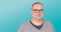 Mann mit Brille vor blauem Hintergrund, lächelnd, grau meliertes Oberteil