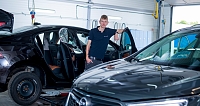 Ein Mechaniker steht neben zwei Autos in einer Werkstatt.