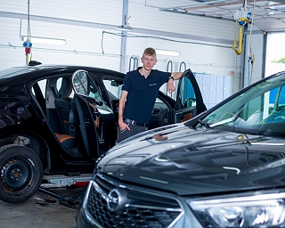 Ein Mechaniker steht neben zwei Autos in einer Werkstatt.