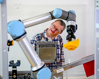 Ein Mensch interagiert mit einem Roboterarm in einer technischen Umgebung.