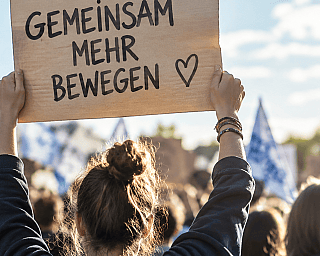 Person hält Plakat mit Botschaft 'Gemeinsam mehr bewegen' auf Demonstration
