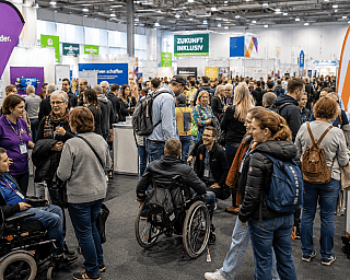 Viele Menschen, darunter Rollstuhlfahrer, auf einer inklusiven Messe in einer Halle
