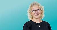 Porträt einer älteren Frau mit Brille vor türkisfarbenem Hintergrund
