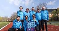 Neun Personen in blauen Jacken posieren auf einer Laufbahn im Freien bei Tageslicht