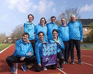 Acht Personen in blauen Sportjacken posieren auf einer Laufbahn im Freien