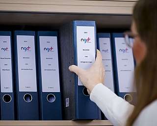 Hand nimmt blauen Ordner aus Regal mit mehreren ähnlichen Ordnern
