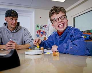 Junger Mann mit Brille lächelt, während er Korken mit bunter Farbe bemalt