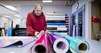 Mann in rotem Kapuzenpullover bearbeitet bunte Folienrollen in Werkstatt