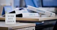 Holzschild auf Schreibtisch mit Text ‚Ab hier bitte lächeln‘ in Büro