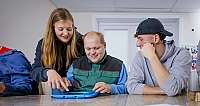 Drei Personen sitzen zusammen und bedienen ein Tablet in einem Raum