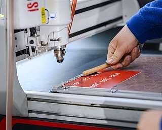 Hand verwendet Holzgriff an einer Maschine zur Bearbeitung eines roten Materials