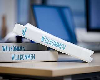 Weiße Bücher mit dem Text Willkommen auf einem Schreibtisch mit verschwommenem Hintergrund