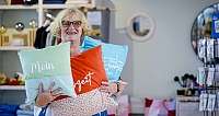 Lächelnde Frau mit Brille hält mehrere bunte Kissen in Geschäft mit Heimdekor