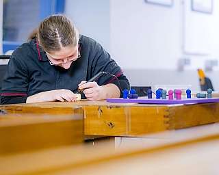 Person arbeitet aufmerksam mit einem Werkzeug an einem Holzstück an einem Tisch