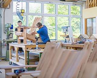 Zwei Männer arbeiten in einer hellen Werkstatt an einem Holzstuhl