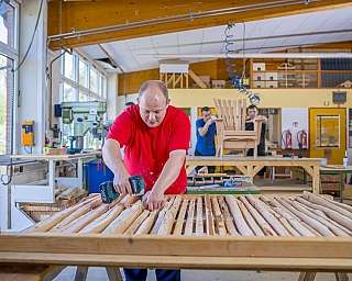 Mann mit rotem T-Shirt arbeitet mit Bohrmaschine an Holzlatten in Werkstatt
