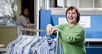 Lächelnde Frau in grünem Pullover mit Kleidung auf einem Kleiderständer in Innenraum