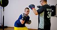 Zwei Männer im Boxtraining in Sportkleidung, einer mit Boxhandschuhen, der andere mit Pratzen