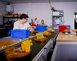 Vier Personen arbeiten an einem Tisch mit gelben und blauen Kunststoffteilen in einer Werkstatt