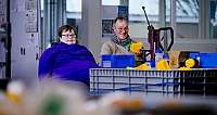Zwei Personen arbeiten an einem Tisch mit gelben und blauen Kunststoffteilen in Werkstatt