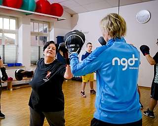Gruppe übt Boxen mit Handschuhen in hellem Trainingsraum mit Holzboden