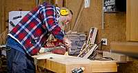 Mann mit Gehörschutz schleift Holz auf Werkbank in Holzwerkstatt