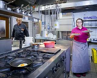 Eine Frau serviert Teller mit Essen in einer professionellen Küchenumgebung