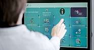 Person berührt Touchscreen mit Informationskacheln auf einem Bildschirm