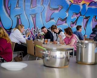 Gruppe von Menschen isst gemeinsam an einem Tisch vor bunter Graffiti-Wand