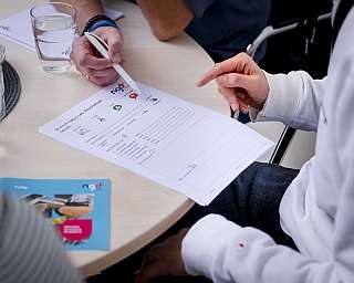 Person füllt Feedbackformular mit Stift auf Tisch mit Glas Wasser aus