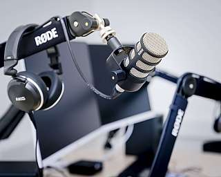Nahaufnahme eines Rode Mikrofons an einem Mikrofonarm mit AKG Kopfhörern im Hintergrund