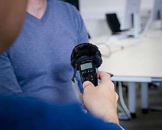 Person hält Aufnahmegerät mit Windschutz vor anderem im Büro