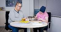 Mann und Jugendliche sitzen an Tisch bei Beschäftigungstherapie mit Holzspielen