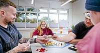 Gruppe von Menschen spielt Brettspiel an einem Tisch in hellem Raum