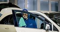 Mann in blauer Kapuzenjacke reinigt Autofenster mit grünem Tuch
