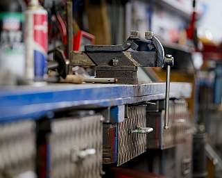 Metallischer Schraubstock auf Werkbank in einer Werkstatt mit Werkzeugen im Hintergrund