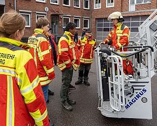 Feuerwehrleute in Schutzkleidung stehen vor Feuerwehrfahrzeug und besprechen Einsatz