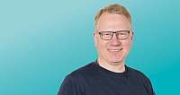 Porträt eines lächelnden Mannes mit blauer Brille vor blauem Hintergrund